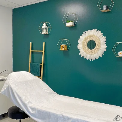 Salle de spa moderne avec mur vert, table de massage et étagères hexagonales décoratives.