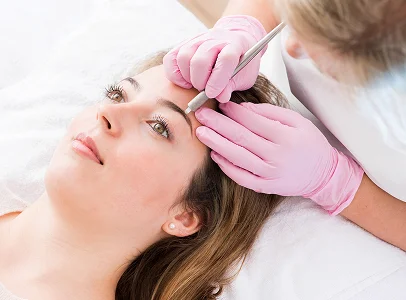 Femme recevant une procédure d'épilation des sourcils par une esthéticienne gantée.